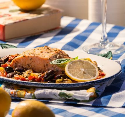 Grilled salmon served with olives, tomatoes, and lemon on a checkered tablecloth.