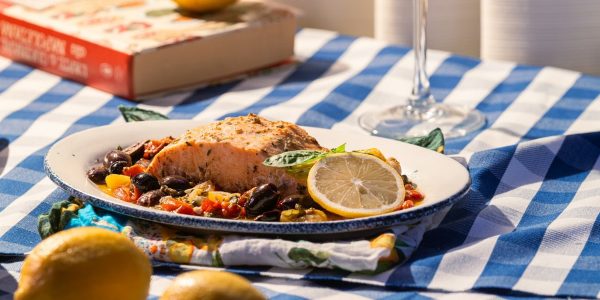 Grilled salmon served with olives, tomatoes, and lemon on a checkered tablecloth.